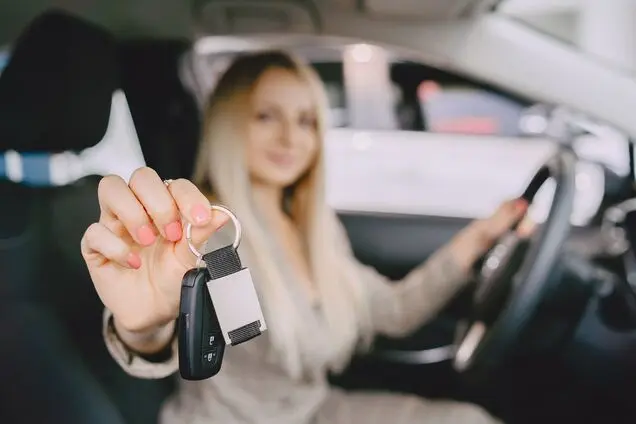 Жінка показує ключі від автомобіля з усмішкою.
