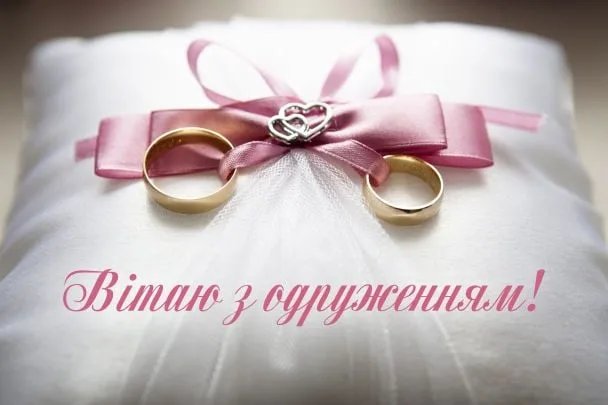 Два золоті обручальні кільця на подушці з рожевою стрічкою