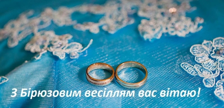 Два весільні кільця на блакитній тканині з квітковим вишивкою.