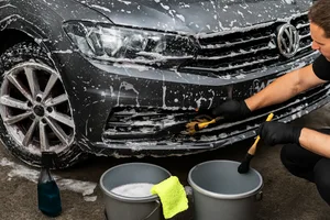 Чоловік миє чорний автомобіль з піною руками.
